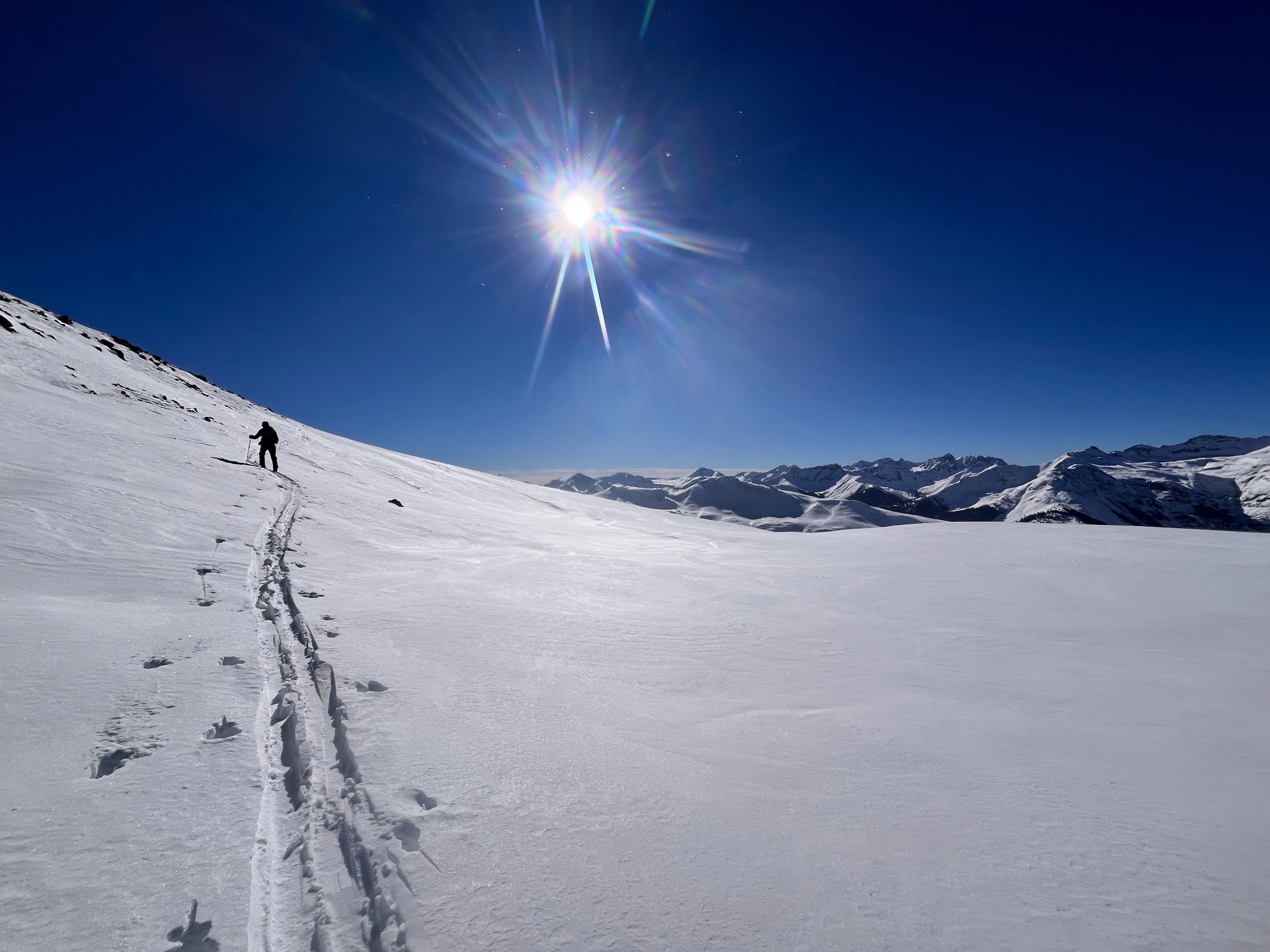 Sunlit snow-covered mountain landscape with a lone skier ascending