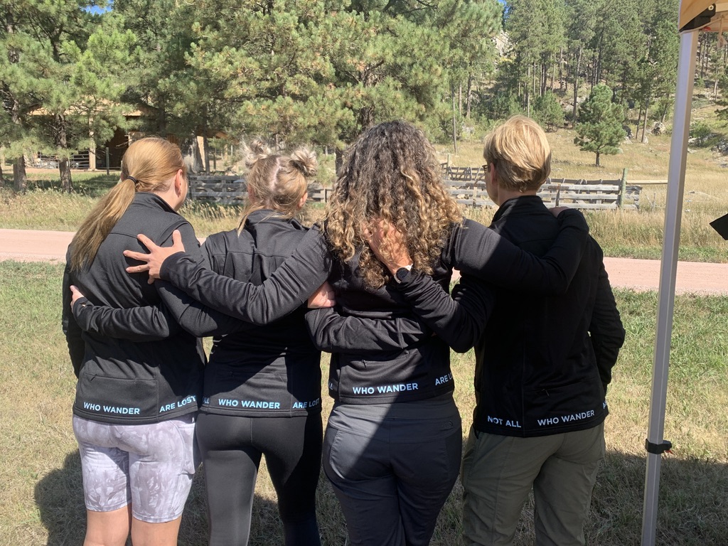 Four people with arms around each other photographed from behind outdoors