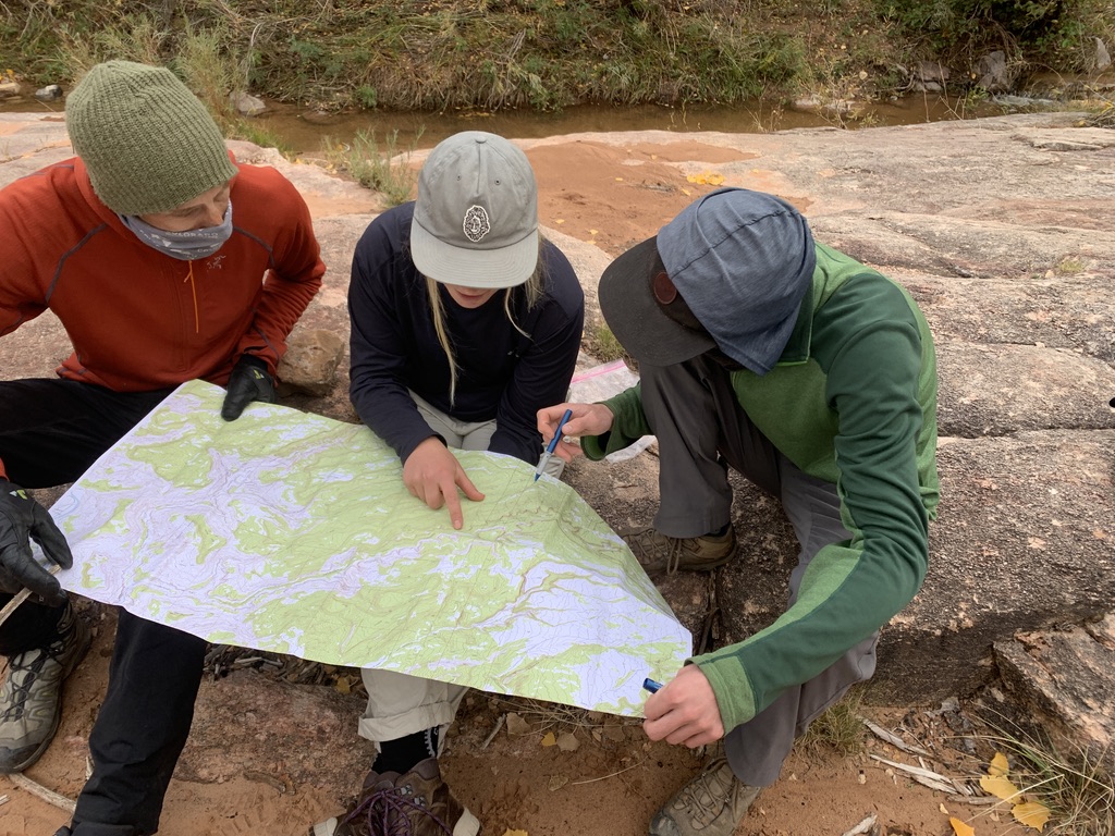 Three people collaborating over a trail map outdoors